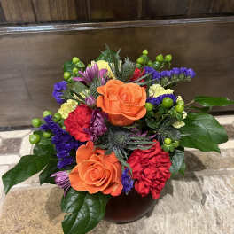 Colorful bouquet with orange roses and purple, red, and yellow flowers in a vase