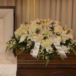 White floral casket spray with lilies and ribbon