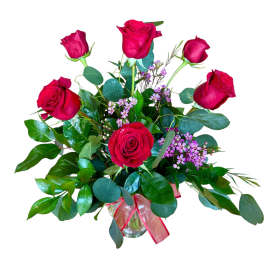 Vase arrangement of red roses with small pink filler flowers in a clear glass vase with red ribbon