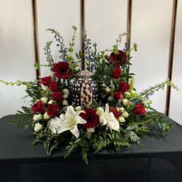 Red roses, white lilies, and gerbera daisies arranged around a patriotic urn