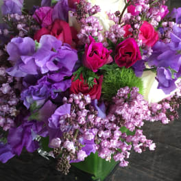 Bouquet of pink, purple, and white roses with lilac blossoms in a green vase