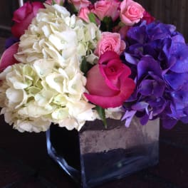 Bouquet of pink roses, white hydrangeas, and purple hydrangeas in a square vase