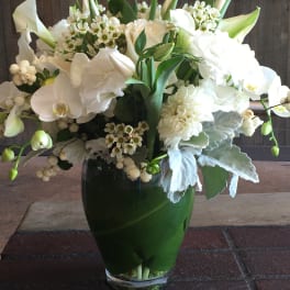 White floral arrangement in a glass vase with orchids and calla lilies