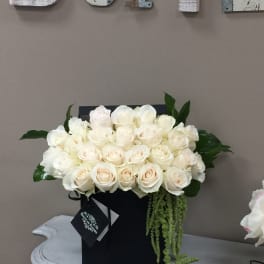 Cream rose arrangement in a black box with trailing greenery