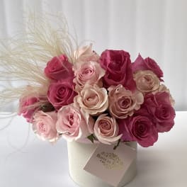 Pink and blush roses arranged in a round box with decorative grass