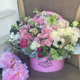 Pink and cream roses arranged in a pink hat box with pastel blooms