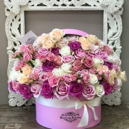 Pink and cream roses arranged in a round hat box with a ribbon