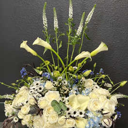 Large white floral arrangement with calla lilies, roses, and blue hydrangeas