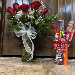 Red roses in a glass vase with a white ribbon and a candy gift box