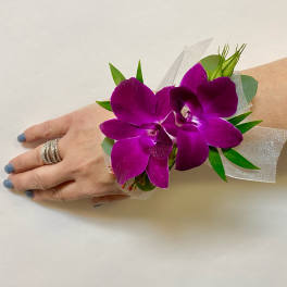 Purple orchid corsage with green accents on a wrist