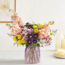 Mixed bouquet in a purple glass vase with pink, yellow, and purple flowers