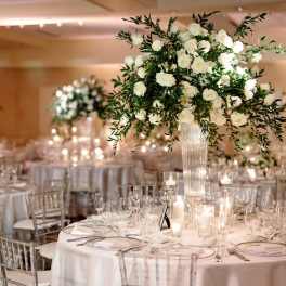 White rose centerpiece in a tall glass vase on a candlelit banquet table