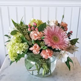 Pink gerbera and peach carnations in a round glass vase