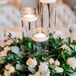 White roses and greenery around three glass candle holders
