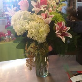 Tall bouquet of white hydrangeas, pink roses, and lilies in a glass vase
