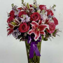 Bouquet of red roses and pink lilies in a glass vase with a purple ribbon