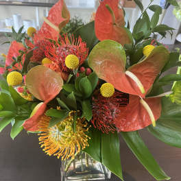 Tropical bouquet with orange anthuriums and yellow pincushion blooms in a glass vase