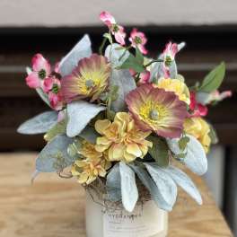 Small floral arrangement in a white container with pink and yellow blooms