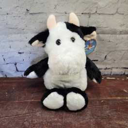 Black-and-white plush cow sitting upright on a wooden surface