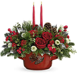 Red roses and holiday greenery in a red container with two red candles