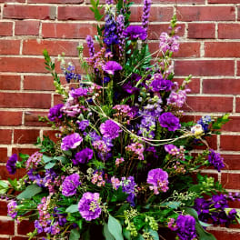 Tall purple floral arrangement in a dark vase