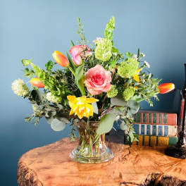 Mixed bouquet of pink roses, tulips, and yellow flowers in a clear glass vase