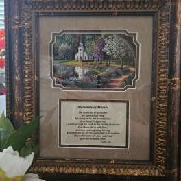 Framed memorial plaque with a church scene and poem, with white flowers at the bottom