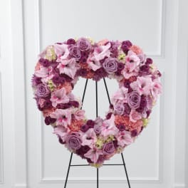 Heart-shaped pink and purple standing wreath of roses, carnations, lilies, and mums on a metal easel
