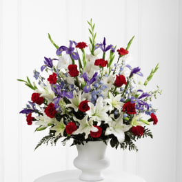 Tall red, white, and purple arrangement with lilies, roses, and irises in a white urn vase