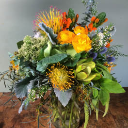 Bright mixed bouquet in a clear glass vase with yellow, orange, and green blooms