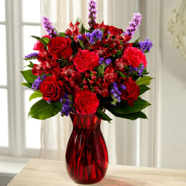 Red and purple flower bouquet in a red glass vase