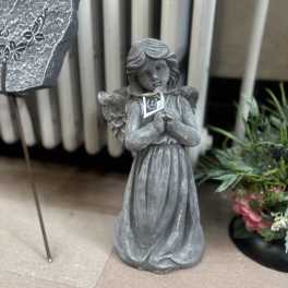 Gray angel statue with clasped hands beside a floral display