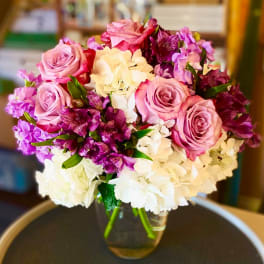 Pink roses and purple flowers arranged with white hydrangeas in a glass vase