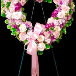 Heart-shaped floral wreath with pink roses and a pink ribbon on a stand