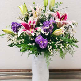 Pink lilies and purple flowers in a white vase with fern accents