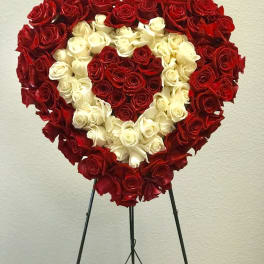 Heart-shaped standing arrangement of red and white roses on a black easel.