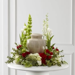 Cremation urn ringed by red roses, white tulips, and white hydrangeas with green accents on a round table