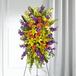 Standing spray of yellow lilies, orange roses, and purple flowers on a metal easel