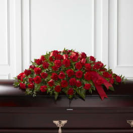 Red rose and carnation casket spray with red ribbon on a dark wood casket