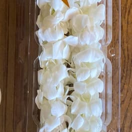 White flower lei in clear plastic packaging with a gold ribbon