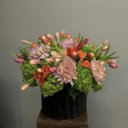 Mixed bouquet of pink tulips, orange roses, and pale chrysanthemums in a black container