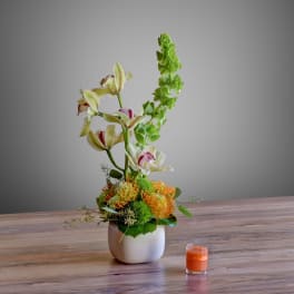 Tall floral arrangement in a white vase with orange and green blooms
