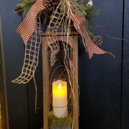 Rustic wooden lantern with glowing candle, pinecones, and plaid ribbon accents