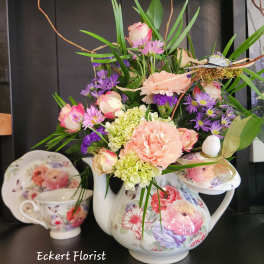 Floral arrangement in a floral teapot with pink, purple, and green blooms