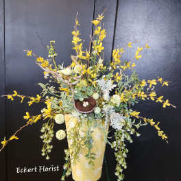 Yellow floral arrangement in a decorative vase with a small bird nest accent