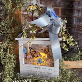 Memorial lantern with white flowers, butterflies, and a silver ribbon