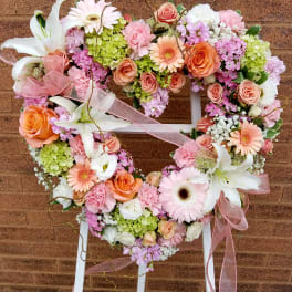 Heart-shaped floral wreath with pink, peach, and white flowers on a stand