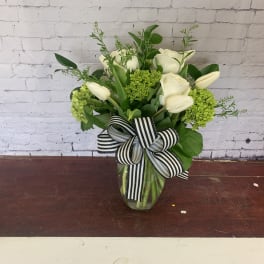 White roses and tulips in a glass vase with a striped ribbon