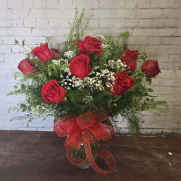 Red roses arranged in a glass vase with baby's breath and a red ribbon