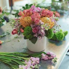 Pink roses and orange pincushion blooms in a white vase